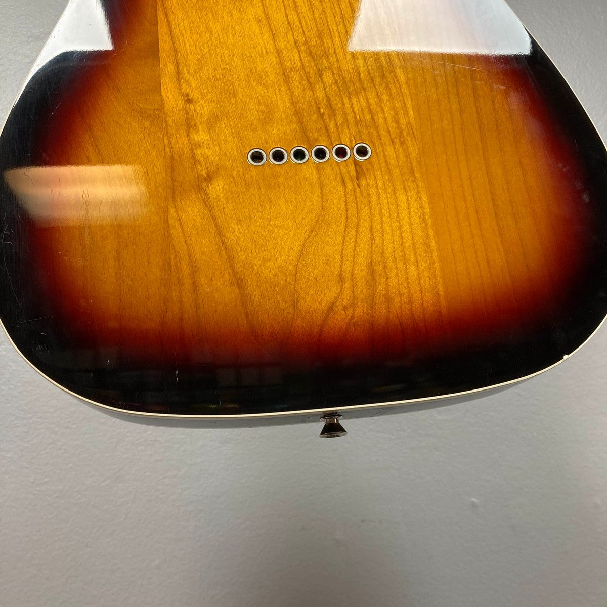 Close-up of the lower body of a sunburst acoustic guitar, highlighting exposed bridge pin holes—echoing classic details of the Fender Heritage '60s Telecaster Custom Made in Japan Sunburst w/Gigbag Consign by Fender.