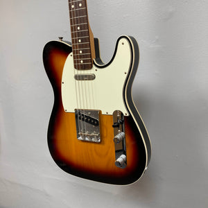 The Fender Heritage '60s Telecaster Custom Made in Japan Sunburst w/Gigbag Consign is shown with a sunburst finish, white pickguard, and two control knobs, hanging against a plain light gray wall.