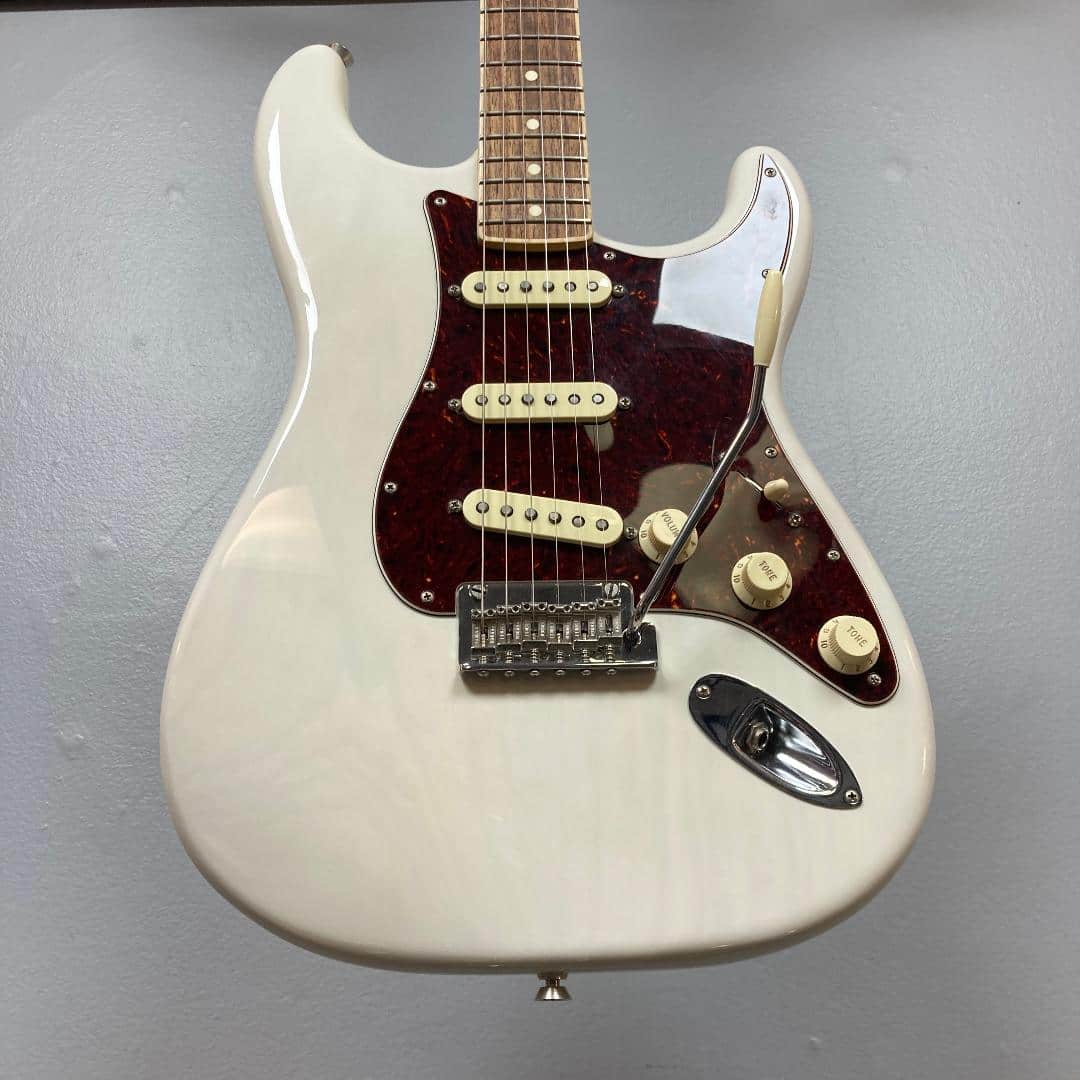 A Fender Limited Edition Ash American Professional Stratocaster in White Blonde with three single-coil pickups, knob controls, brown pickguard, and tremolo arm is shown against a gray background.