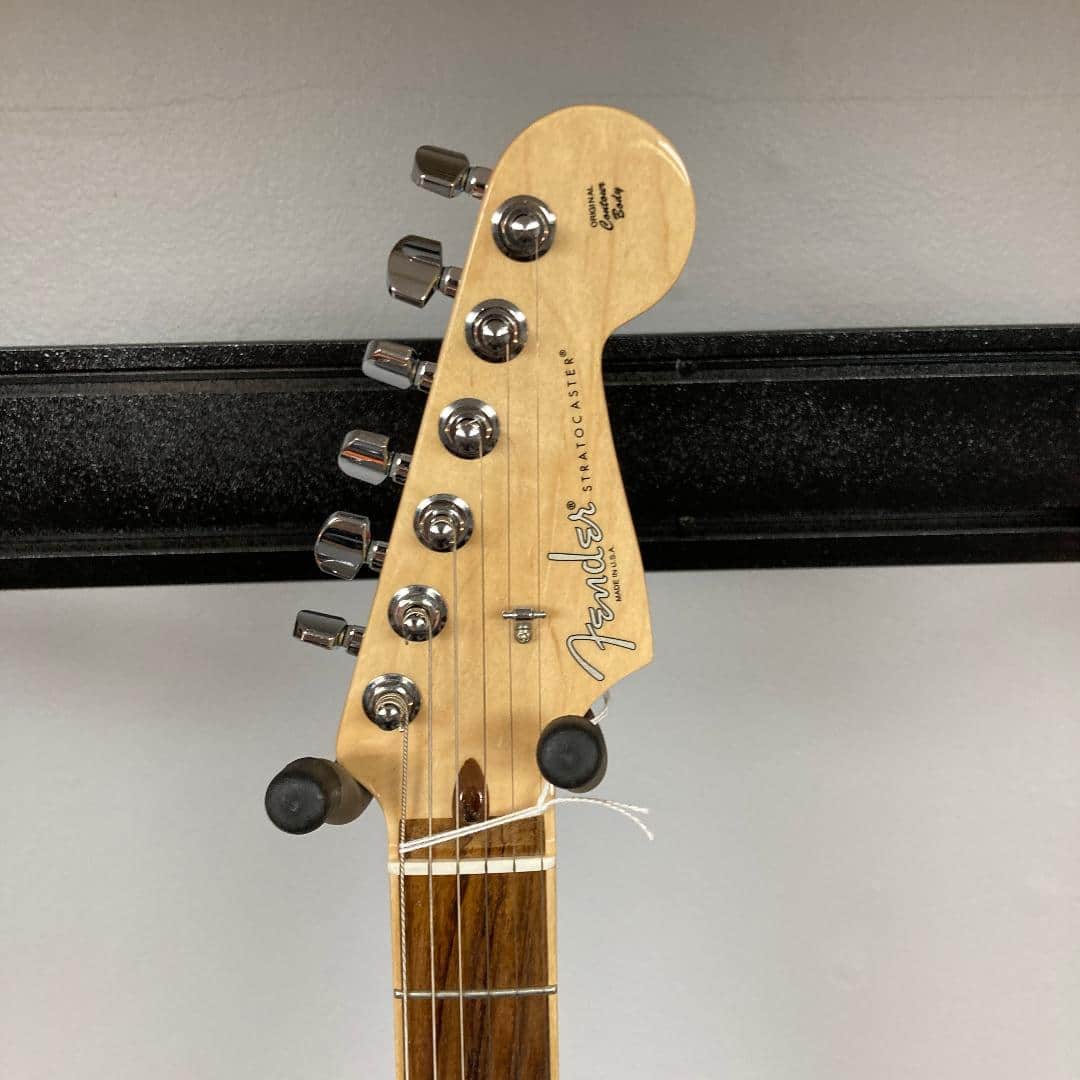 Close-up of a Fender Limited Edition Ash American Professional Stratocaster in White Blonde, highlighting six tuning pegs, visible strings, and part of a wall-mounted hanger. The channel-bound neck reflects Fender’s refined craftsmanship.