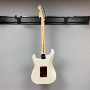 A Fender Limited Edition Ash American Professional Stratocaster White Blonde w/Case Consign is displayed from the back, hanging on a black metal wall rack against a plain light gray wall.