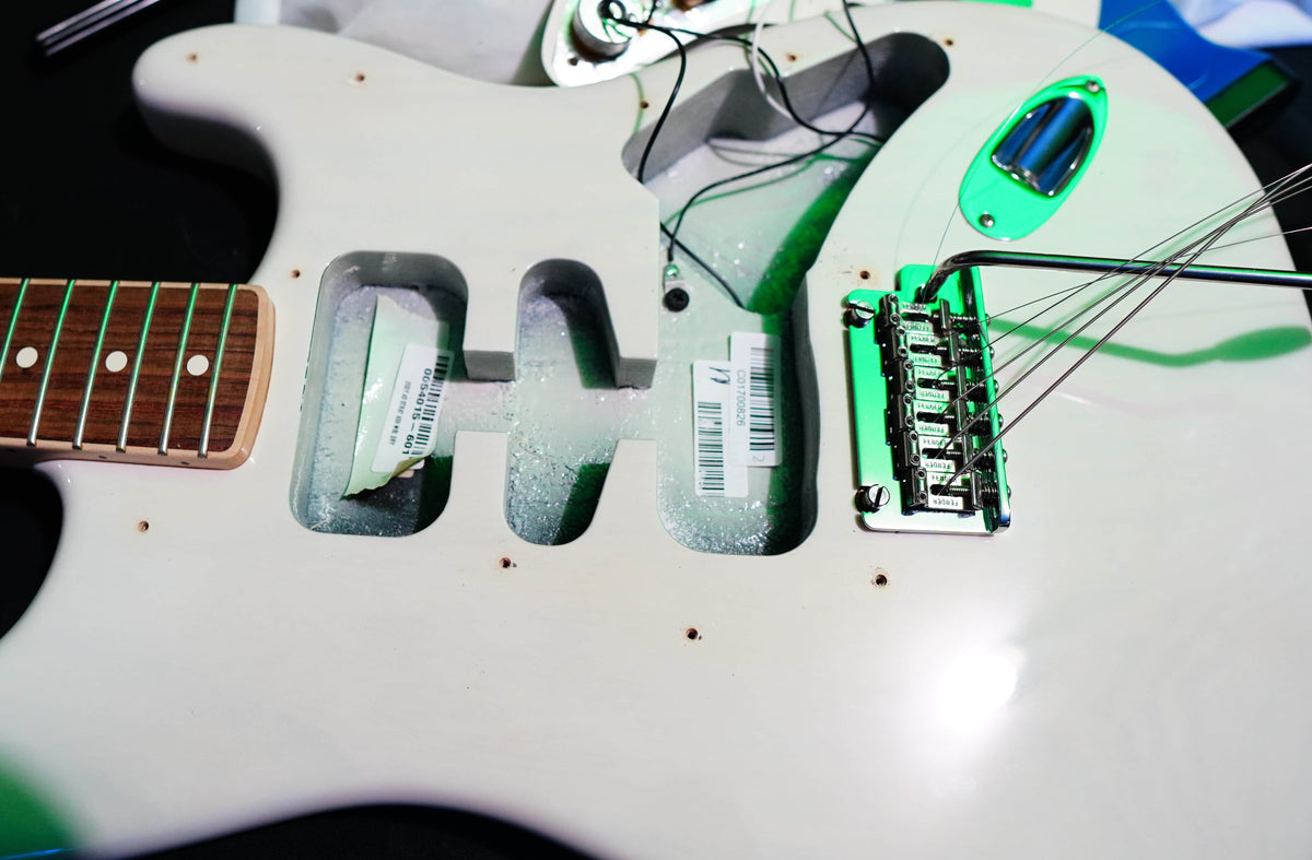 Close-up of a Fender Limited Edition Ash American Professional Stratocaster White Blonde body, showing exposed cavities, bridge, loose strings, visible pickup covers, and wiring; by Fender.