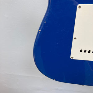 Back of a blue Fender MIM Stratocaster guitar, showing finish blemishes and a screw in the surface.