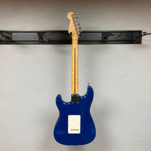 Fender MIM Stratocaster Blue 1998 with a wooden neck, white pickguard, and three pickups, displayed on a wall. Used condition with case included.