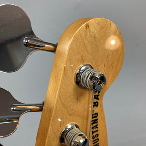 Close-up of a Fender Mustang Player Bass PJ White Used headstock by Fender, featuring two chrome tuning pegs and part of the "MUSTANG BASS" logo on a plain gray background. This short scale bass offers comfortable, punchy playability.