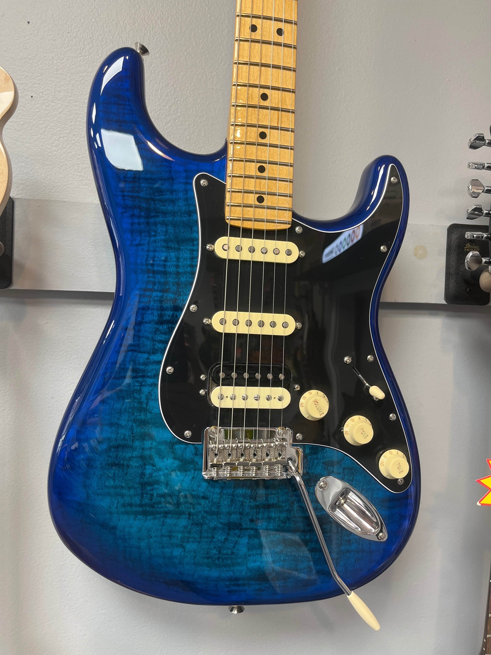 A used Fender Player II Stratocaster HSS Plus Top in Blue Burst with a maple fingerboard, black pickguard, HSS pickups, and a tremolo bridge is wall-mounted for display.