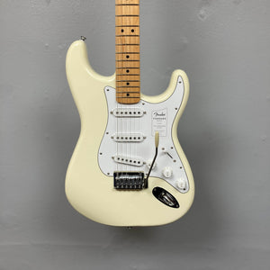 A Fender Standard Stratocaster Olympic White Refurb guitar by Fender, featuring a maple neck and three single-coil pickups, hangs against a plain gray wall.