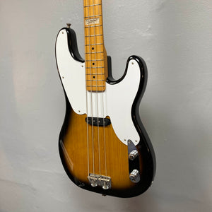 The Fender Sting P Bass Sunburst by Fender, featuring a white pickguard and maple neck, is photographed against a plain light gray wall, highlighting its classic vintage-style electric bass design.