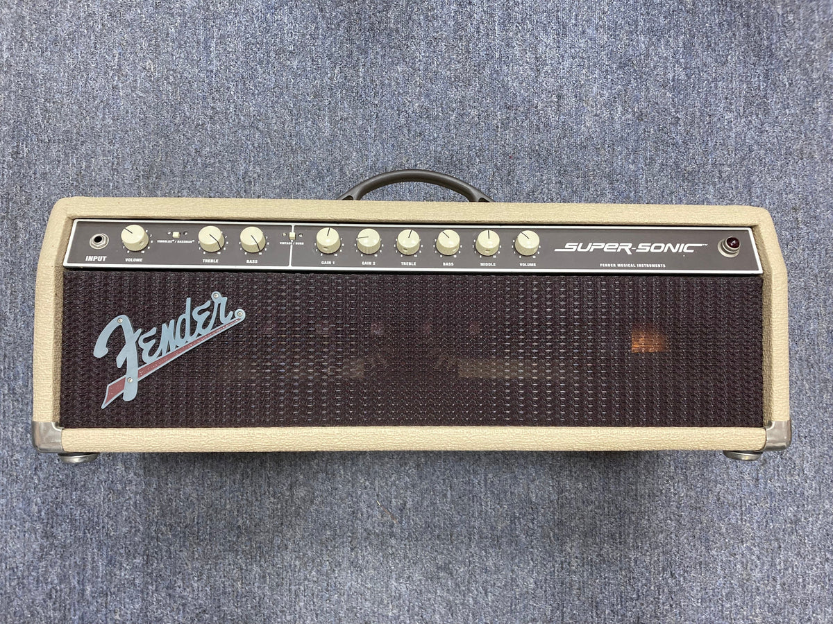 Fender Super-Sonic 60-Watt Amp Head on a carpet, showcasing its knobs and logo in close-up.