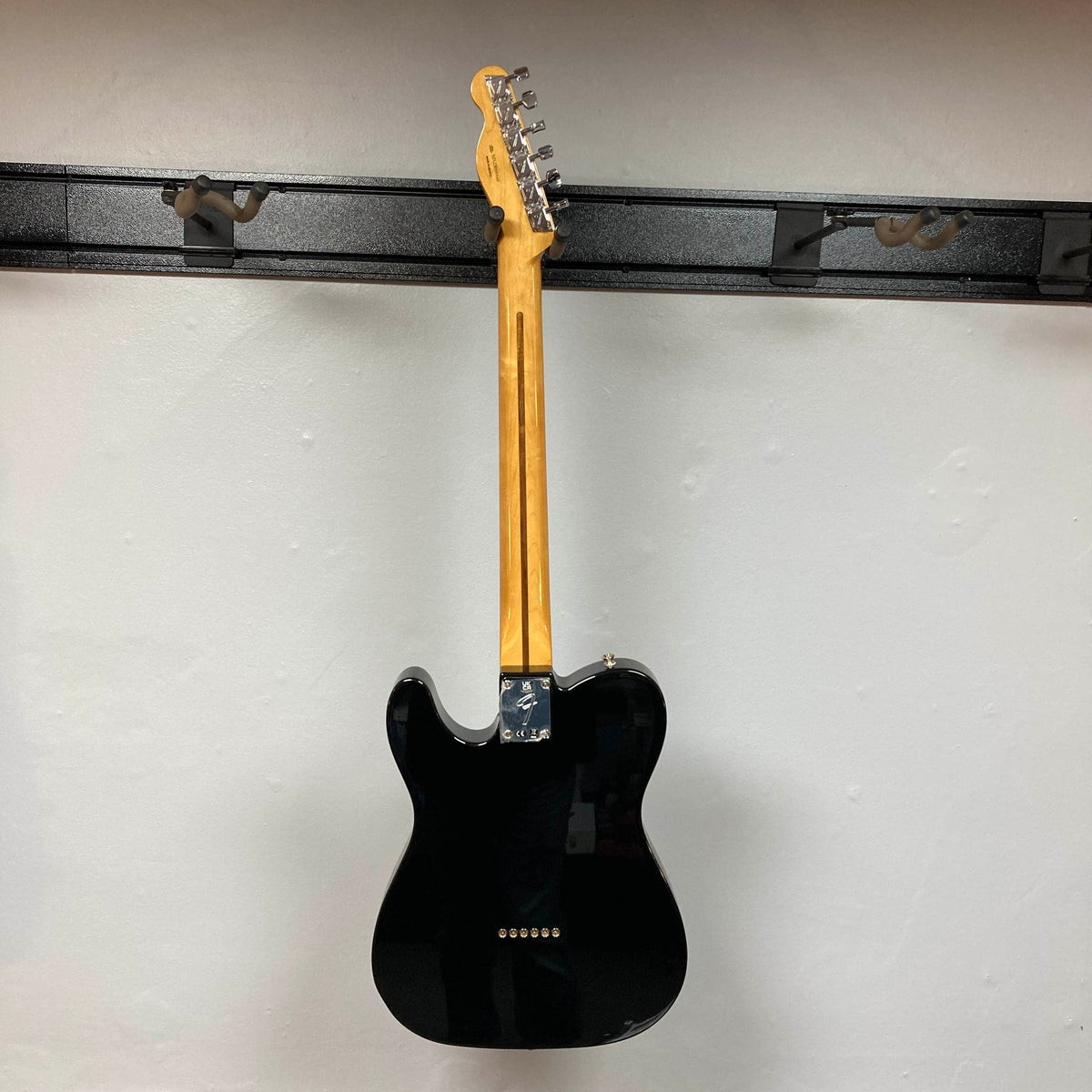 A Fender Vintera II ’60s Telecaster Thinline in black is hanging on a wall with its back facing outward. This eye-catching Fender guitar boasts a semi-hollow ash body and vintage-style Tele pickups, true to the classic ’60s design.