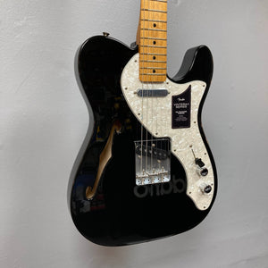 A Fender Vintera II ’60s Telecaster Thinline Black Used electric guitar by Fender, featuring a white pearl pickguard, maple neck, vintage-style Tele pickups, and an f-hole, graces the wall. Its semi-hollow ash body enhances both its classic appearance and resonant tone.