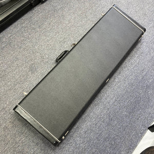 A black hard case with metal latches and a handle sits on a gray carpet, ideal for safely storing your G&L L-2000 USA Tobacco Sunburst Bass (Used Consign).