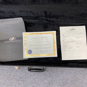 A certificate of authenticity, spec sheet, and black envelope are shown inside an open G&L L-2000 USA Tobacco Sunburst Bass w/Case Used Consign on a gray carpet, highlighting its classic finish.
