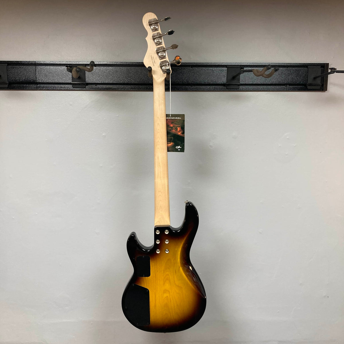 A G&L L-2000 USA Tobacco Sunburst Bass w/Case (used, consignment) by G&L is shown hanging on a wall rack, displayed from the back with its tag attached to the headstock.