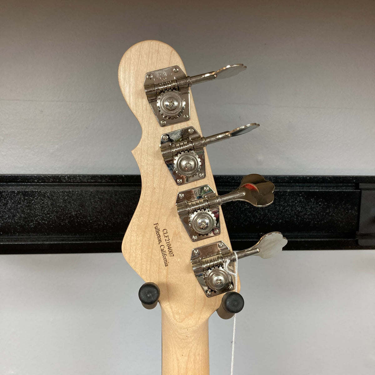 The back of a G&L L-2000 USA Tobacco Sunburst Bass w/Case Used Consign headstock shows four tuning pegs as it hangs on a wall-mounted holder.