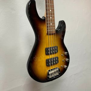 A G&L L-2000 USA Tobacco Sunburst Bass w/Case (used, consignment), featuring two pickups, four control knobs, and a chrome bridge, hangs on a white wall.