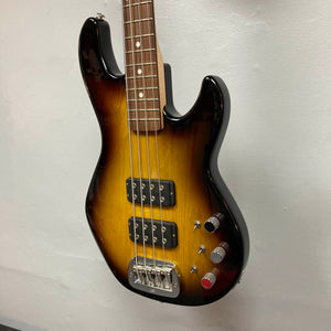 A G&L L-2000 USA Tobacco Sunburst Bass w/Case Used Consign, featuring four strings, two humbuckers, and three control knobs, is mounted on a white wall.
