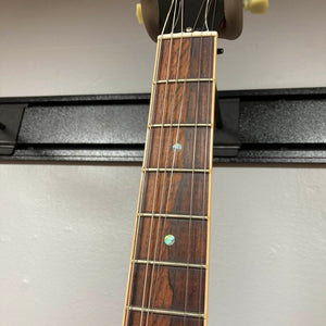 Close-up of the Gibson Custom Shop Class 5 Les Paul’s flame maple fretboard with metal frets, dot inlays, and loose strings against a light wall—showcasing Gibson craftsmanship.