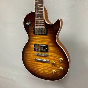 A Gibson Custom Shop Class 5 Les Paul electric guitar with a sunburst finish, single-cutaway body, dual humbuckers, four gold knobs, and a flame maple top hangs on a light gray wall.