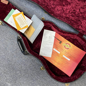An open guitar case with red velvet lining displays documents including a certificate of authenticity for a Gibson Custom Shop Class 5 Les Paul by Gibson, plus checklists and envelopes, all arranged inside on a gray carpet.