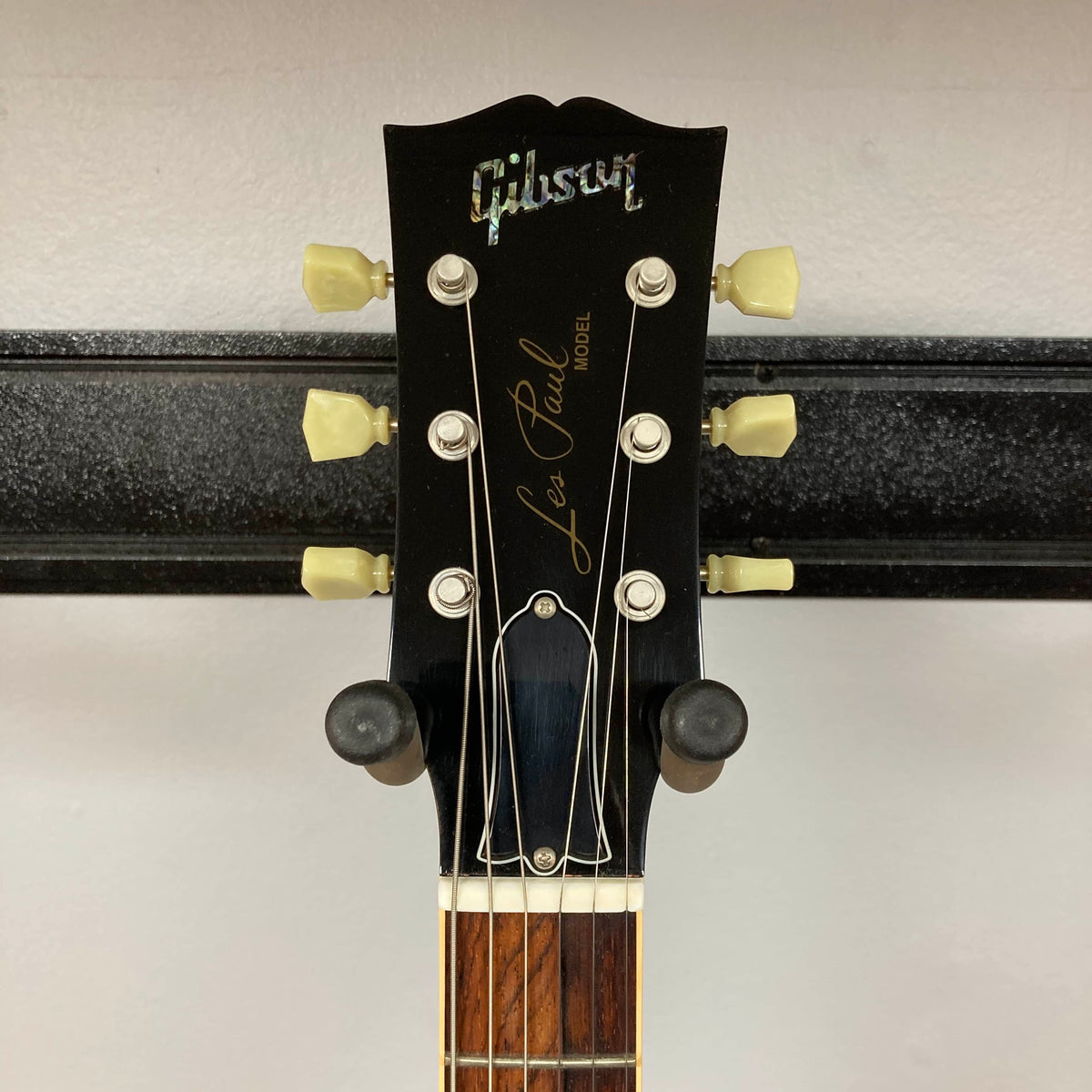 Close-up of the headstock of a Gibson Custom Shop Class 5 Les Paul by Gibson, showing tuning pegs, logo, and part of the fretboard against a white wall background.
