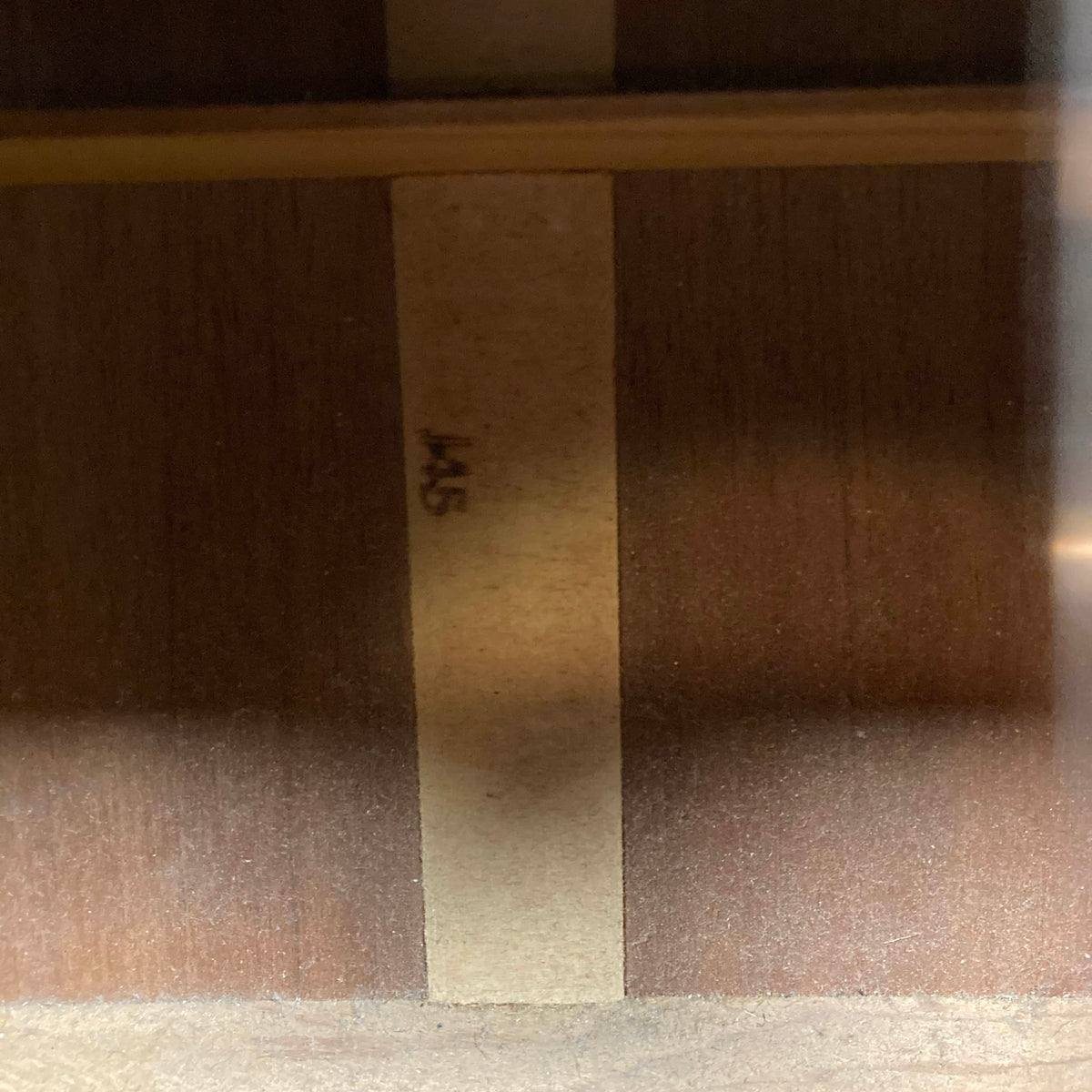 Wooden surface with vertical strips and “145” on a lighter strip, echoing the timeless design of the Gibson J-45 1957 Serial U-8664-1 by Gibson—classic charm reimagined.