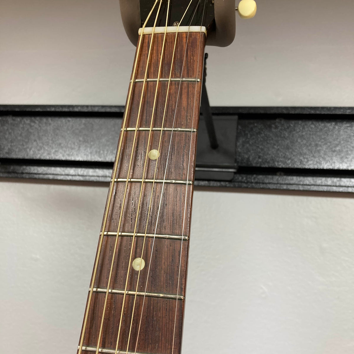 Close-up of the Gibson J-45 1957 (Serial U-8664-1) guitar neck by Gibson, highlighting six strings, metal frets, and two white dot inlays on its dark wooden fretboard.
