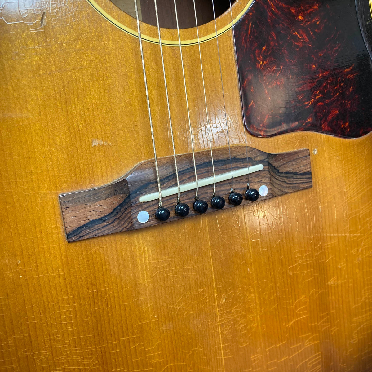 Close-up of the Gibson J-45 1957 Serial U-8664-1 bridge and strings, highlighting the wood grain, bridge pins, and visible wear—classic details of this vintage Gibson acoustic guitar.