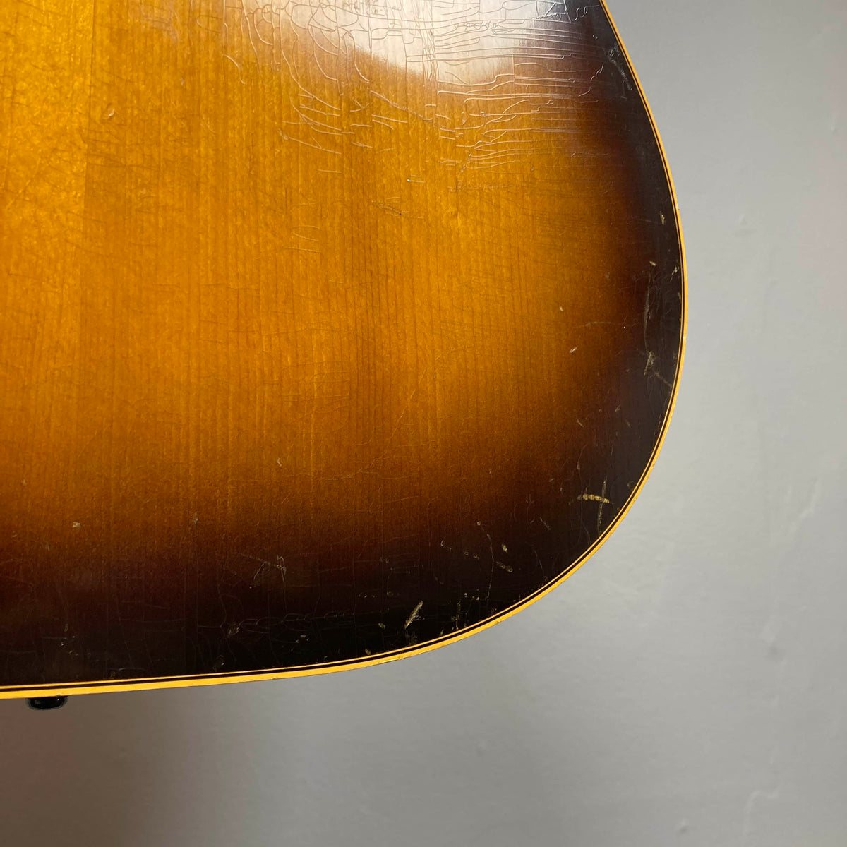 Close-up of the lower body of a Gibson J-45 1957 Serial U-8664-1 acoustic guitar, featuring a sunburst finish, visible surface scratches, and a light-colored outline set against a plain background.