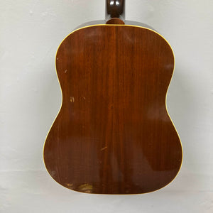 Back view of a Gibson J-45 1957 (Serial U-8664-1) acoustic guitar with a glossy finish, visible scratches, and yellow edge binding. The classic slope shoulder design is set against a light-colored wall.