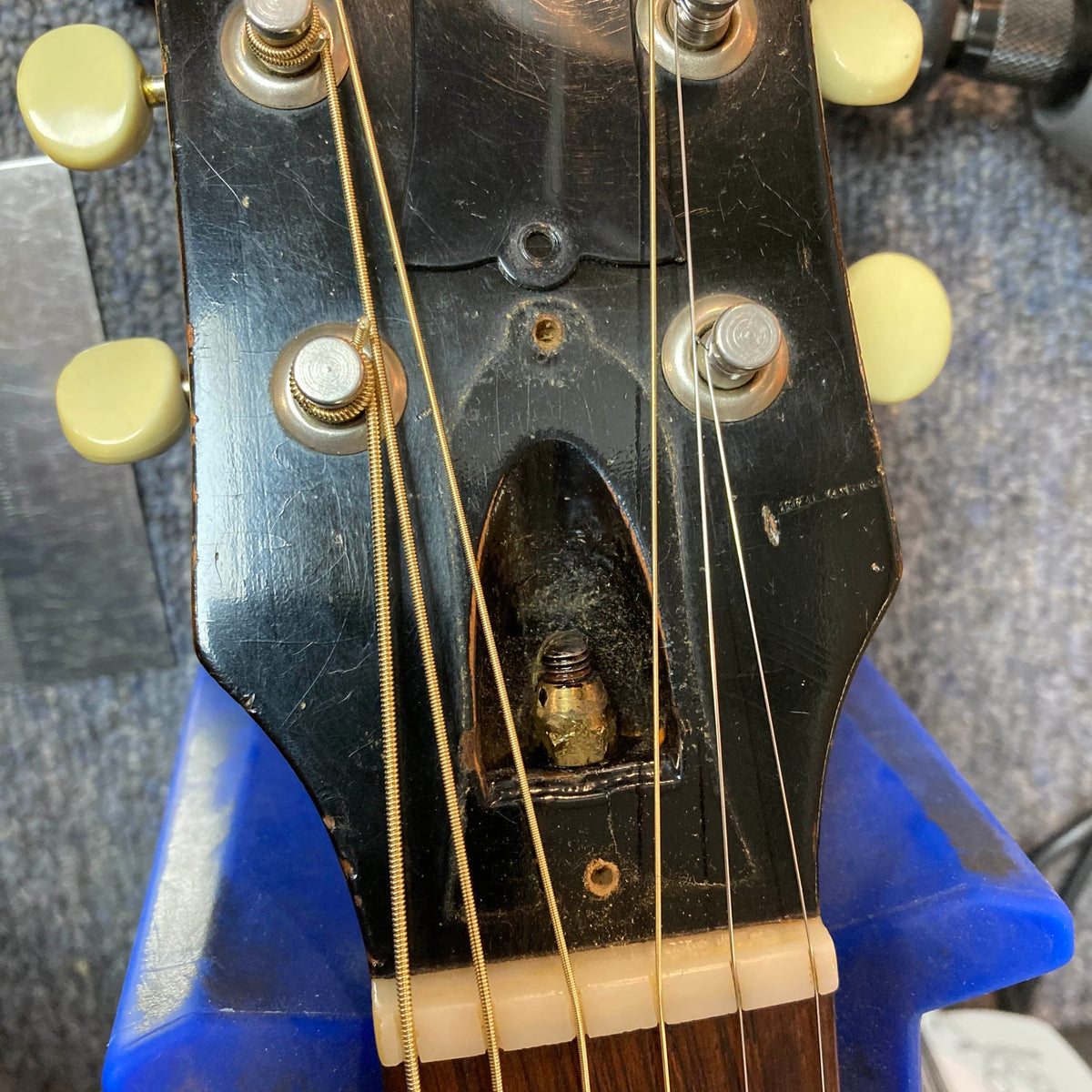 Close-up of the Gibson J-45 1957 (Serial U-8664-1) headstock, highlighting tuning pegs, strings, truss rod access cavity, and part of a blue guitar support—iconic vintage style by Gibson.
