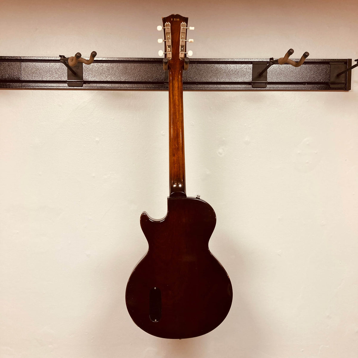 A Gibson Les Paul Junior 1957 Sunburst electric guitar by Gibson hangs by its neck on a wall rack, displayed with its back facing outward.