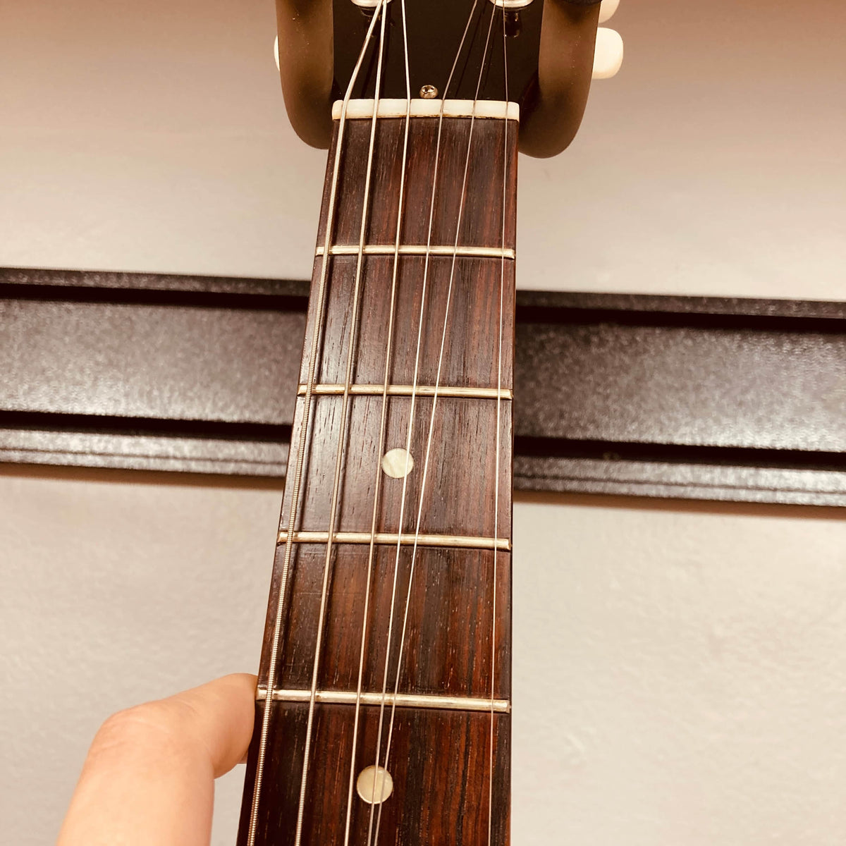 Close-up of a hand pressing a string on the fretboard of a Gibson Les Paul Junior 1957 Sunburst electric guitar by Gibson, held vertically in front of a beige wall.