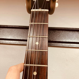Close-up of a hand pressing a string on the fretboard of a Gibson Les Paul Junior 1957 Sunburst electric guitar by Gibson, held vertically in front of a beige wall.