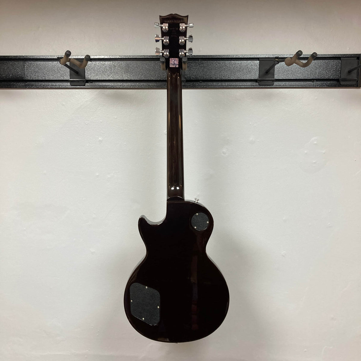 A Gibson Les Paul Studio 2015 Desert Burst electric guitar by Gibson, shown from the back on a wall mount with locking tuners and rear access panels—an upgraded instrument for serious players. Includes case.