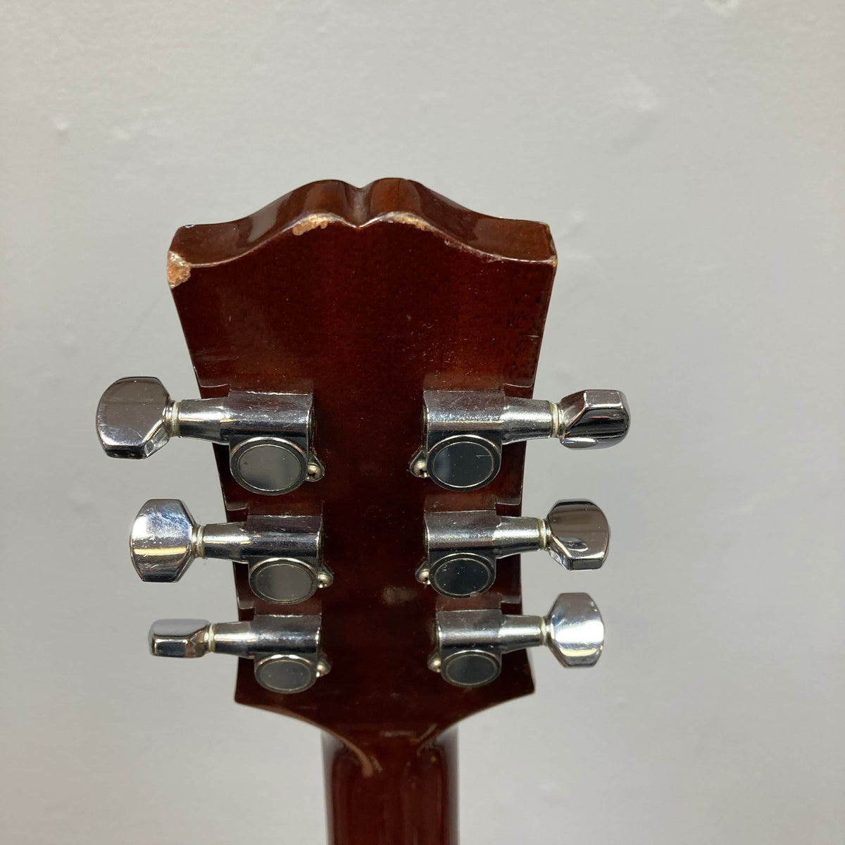 Close-up of the back of a Gibson Nouveau NV6-R 1986 headstock, showing six metal tuning pegs and a worn edge on its brown wood—evoking the classic square shoulder dreadnought style.