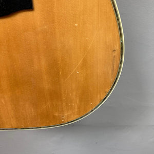Close-up of a Gibson Nouveau NV6-R 1986 acoustic guitar by Gibson, highlighting the wood grain, light scratches, and minor dents on the body edge against a gray background.