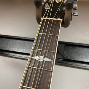 Close-up of a Gibson Nouveau NV6-R 1986 by Gibson, showing the six-string neck, frets, and pearloid inlay on the dark wood fretboard. This vintage acoustic square shoulder dreadnought rests on a wall-mounted holder.