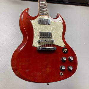 A Gibson SG Standard Heritage Cherry electric guitar (year 2000, Consign) is hanging on the wall, featuring a white pickguard and four control knobs.