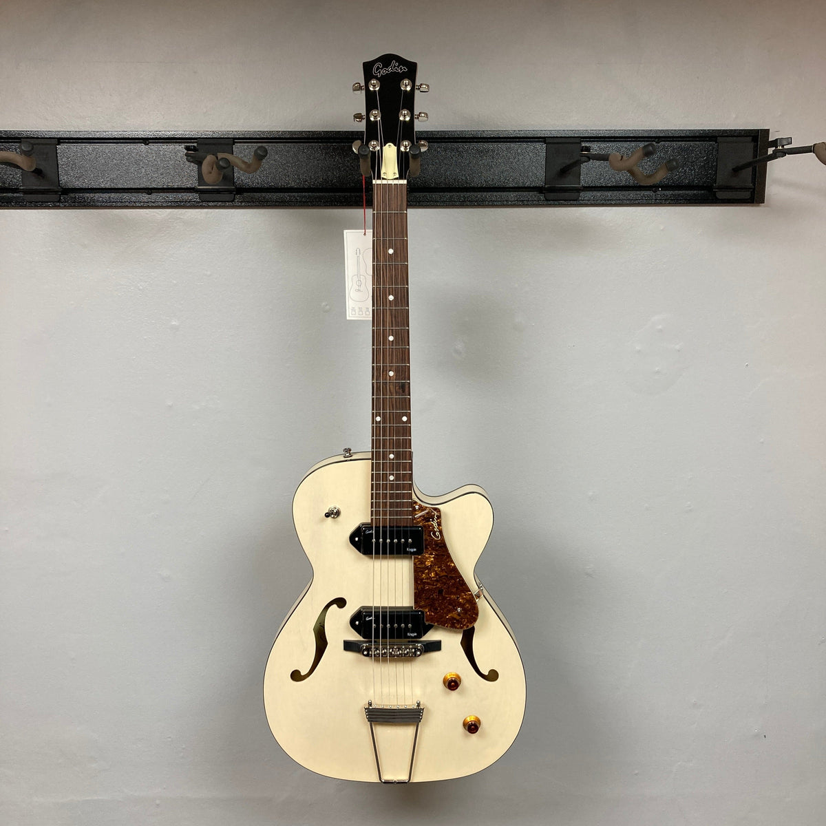 Godin 5th Ave TL Kingpin P90 Trans Cream HG electric guitar displayed on a wall, showcasing its elegant design and craftsmanship.