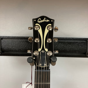 Godin 5th Ave TL Vintage Burst HG Gold Foil guitar on stand, showcasing its hollow body design and neck, ideal for versatile musical genres.