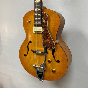 Godin 5th Avenue Jumbo P-Rail Harvest Gold guitar with a classic archtop design and vintage-style features, displayed on a wall.