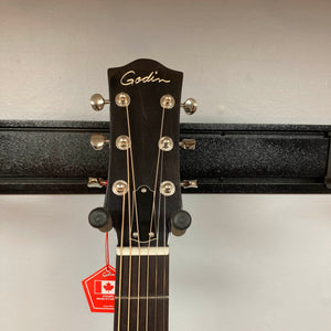 Close-up of the headstock of a Godin Century Maho Rustic Burst EQ SF dreadnought acoustic-electric guitar by Godin, with tuning pegs clearly visible as it hangs on a wall mount. A red tag is attached to one of the tuning pegs, drawing attention to this finely crafted solid wood instrument.