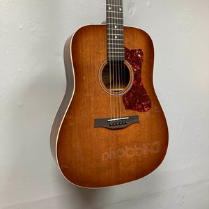 A Godin Century Maho Rustic Burst EQ SF acoustic electric guitar with a tortoiseshell pickguard is hanging on a light-colored wall.