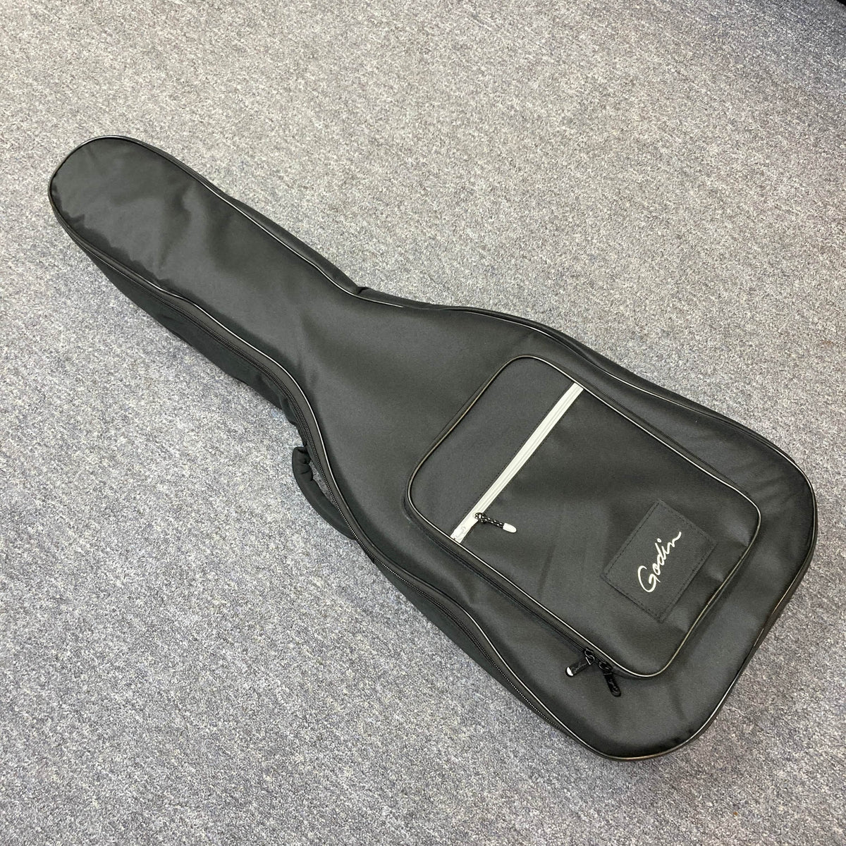 A black Godin gigbag with a zippered front pocket and logo, designed for the Imperial Laguna Blue GT EQ SF Acoustic Guitar, is lying closed on a light gray carpeted floor.
