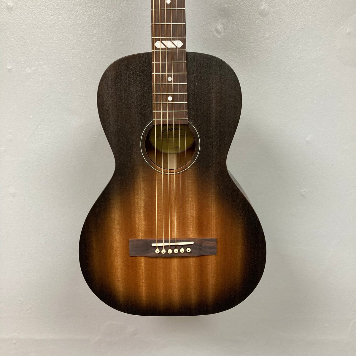 Godin Mahogany Parlor Black Burst A/E guitar with solid Mahogany top and back, displayed on a wall, showcasing detailed strings and craftsmanship.