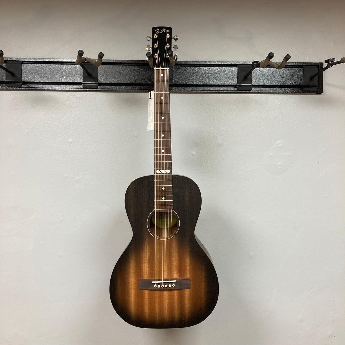 Godin Mahogany Parlor Black Burst A/E guitar mounted on a wall, showcasing its solid mahogany body and Fishman Presys VT system.