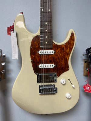 A cream Godin Session T-Pro with Bag electric guitar by Godin, featuring a tortoiseshell pickguard, H-S-S pickups, selector switch, and two knobs, is displayed on the wall.