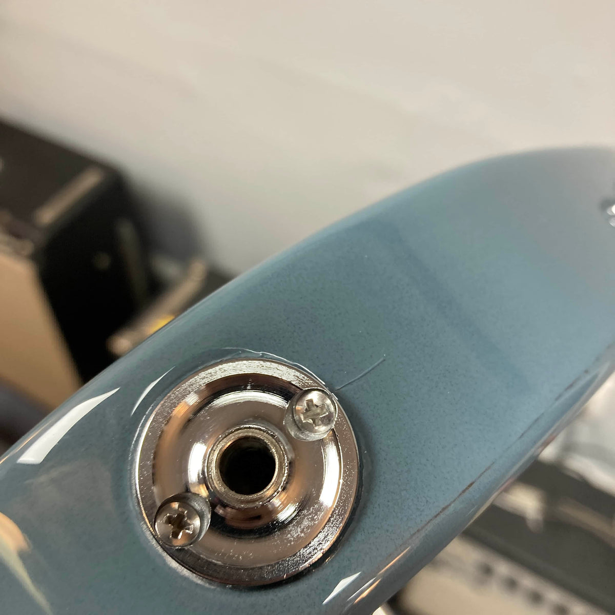 Close-up of the input jack on a metallic blue Godin Session T-Pro with Bag by Godin, featuring an H-S-S pickup configuration and a slight paint crack near the mounting plate.