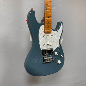 A Godin Session T-Pro electric guitar with a maple neck, white pearloid pickguard, H-S-S pickups, and a tremolo bridge hangs against a plain gray wall. Comes with a branded bag.